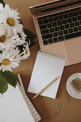 Wall Mural - Home office desk workspace with laptop computer, spiral flip notebook, daisy flowers bouquet on neutral brown background. Flat lay, top view blog, website, social media concept