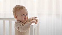 Crying Baby Portrait. Little Infant Tired And Hungry, Start Crying Standing In Crib, Looking Aside At Empty Space