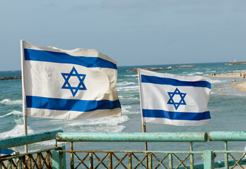 Wall Mural - Large, blue and white flags of the State of Israel rippling in the wind on a sunny day along the shoreline of the Mediterranean Sea.