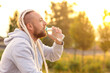 © Eno1 - In the morning at sunrise, a man with an interesting braid hairstyle drinks water from a bottle after a workout