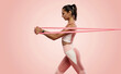 © opolja - Sportswoman exercising with resistance band. Female with working out with elastic band on pink background