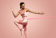 © opolja - Sportswoman exercising with resistance band. Female with working out with elastic band on pink background