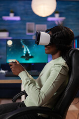 Wall Mural - Concentrated african american streamer woman wearing virtual reality headset playing space shooter videogames using gaming controller during online tournament. RGB computer equipment. Cyber space