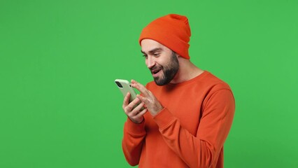 Wall Mural - Happy fun young brunet man 20s years old wears red shirt hat hold use mobile cell phone typing browsing swipe chatting send sms doing online shopping isolated on plain light green background studio