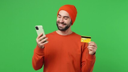 Wall Mural - Happy young brunet man 20s years old wears red shirt hat using mobile cell phone hold in hand credit bank card doing online shopping order booking tour isolated on plain light green background studio