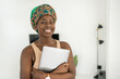 Portrait African woman at home, smiling holding laptop, wearing headscarf