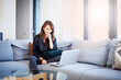 © sepy - Smiling woman relaxining on the sofa at home and using her laptop