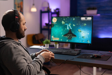 Wall Mural - Person playing video games with joystick and headset on computer. Player using controller and audio headphones for online gaming. Gamer having fun activity with equipment to play games.