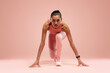 © opolja - Fit young woman standing in start position over pink background. Sportswoman about to start a run