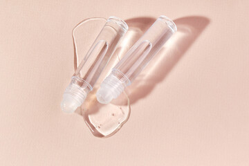 Transparent lip gloss in a roller ball bottles on a beige background. Decorative cosmetic lipstick. Beauty makeup product 