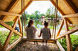 Two little girl то swing in wooden cabin by lake on summer day. Children in nature.