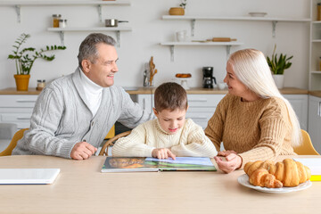 Wall Mural - Little boy with his grandparents in warm sweaters reading book at home