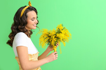 Wall Mural - Beautiful young woman with bouquet of mimosa flowers on green background