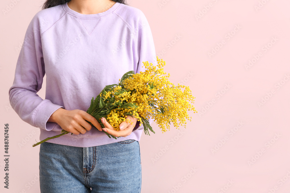 Woman holding beautiful mimosa branches on color background