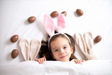 Wall Mural - happy easter. portrait of a cute beautiful girl with blue eyes and rabbit ears. chocolate eggs are s