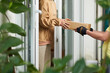 © DragonImages - Close-up of woman opening the door of the house and receiving the parcel from delivery person