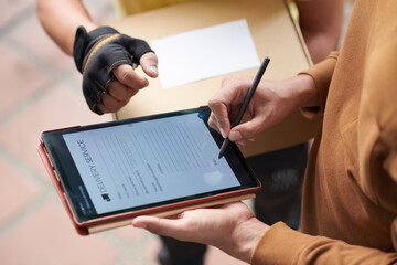 Wall Mural - Close-up of man signing the form on digital tablet while getting the parcel from delivery person