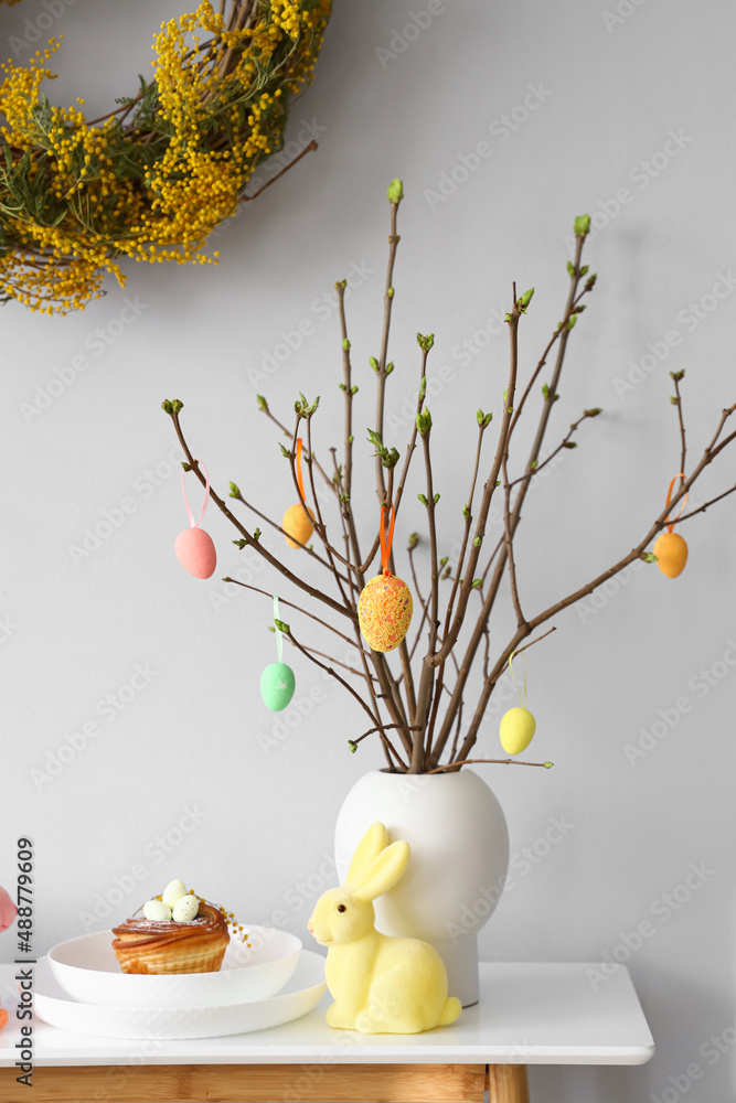 Plate with delicious bun and stylish Easter decor on table near light wall