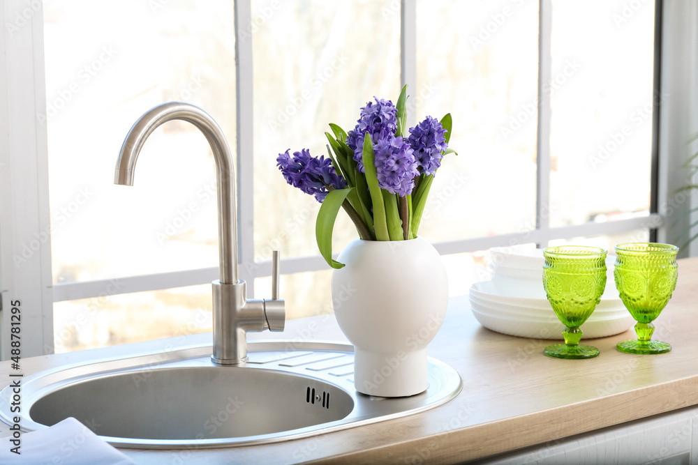 Kitchen counter with modern sink, vase with flowers and dishware near window