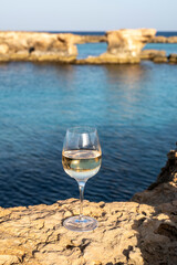 Wall Mural - Glass of cold white dry white wine served on rocks in blue sea bay near Protaras touristic town on Cyprus