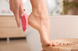 © New Africa - Woman using pumice stone for removing dead skin from feet in bathroom, closeup