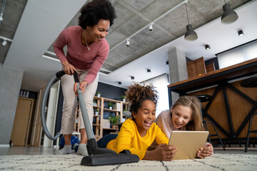 Wall Mural - portrait of happy mother doing household while children having fun with gadgets at home