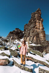 Wall Mural - Russia. Sheregesh. Girl snowboarder in black sun goggles in winter in sunny weather outdoors among the Christmas tree and snow. The girl is standing with a snowboard in her hands and posing. 