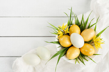 Wall Mural - Easter yellow eggs and bright spring flowers with grass in a bowl on a white table background, top view, copy space. Festive decor, easter card