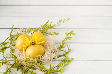 Wall Mural - Easter yellow eggs in a decorative nest decorated with bright spring flowers and willow green branches on a white table background, top view, copy space. Festive decor, easter card