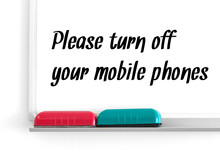 Please Turn Off Your Mobile Phones Written With Black Marker On Whiteboard With Red And Turquoise Cleaning Sponges.