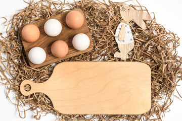 Wall Mural - Easter mockup wood cutting board with bunny and easter eggs on wooden bowl on white background. Flat lay, top view, copyspace.