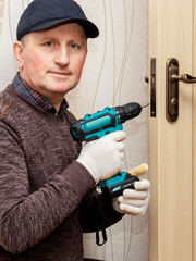 Wall Mural - Craftsman with an electric screwdriver in his hands at the door