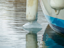 Icy White Fenders Suspended Between A Boat And Dockside For Protection. Maritime Fenders In Winter.