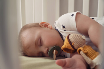 Poster - Adorable little baby with pacifier and toy sleeping in crib, closeup