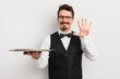 © kues1 - young handsome man smiling and looking friendly, showing number five. waiter and tray concept