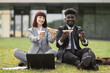 © sofiko14 - Handsome African-American businessman and his female Caucasian colleague, eating lunch sandwiches outside office. Two young business people having lunch break together, sitting on the grass outdoors