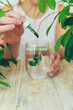 Woman dripping chlorophyll supplement into a glass of water. Selective focus.