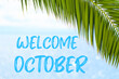 Welcome October text on the background with palm leaf and blue sea. Template of a greeting card, postcard or advertisement of a tour agency. 