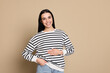 Happy healthy woman touching her belly on beige background