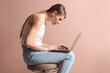 Woman with bad posture using laptop while sitting on stool against pale pink background