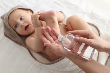 Wall Mural - Mother with bottle of massage oil near baby on bed, closeup