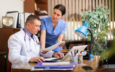 Wall Mural - Two doctors man and woman analysing and consulting over medical record in modern hospital