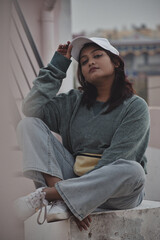 Poster - Beautiful shot of a south asian girl in jeans and a sweater with a white cap sitting outdoors