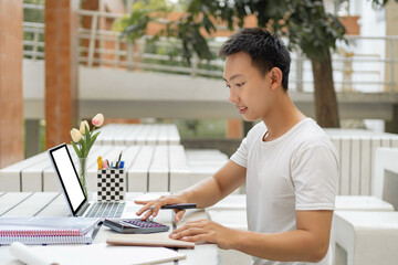 Canvas Print - Online studying concept a male student in white t-shirt studying online by using his new white laptop and the calculator in the accounting class