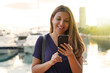 © zigres - Tourist girl scrolling on smartphone touch screen looking for hotel. Traveler woman typing on mobile phone booking a room for the night. Last minute travels concept.