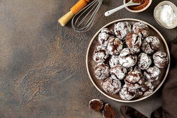 Wall Mural - Homemade chocolate and coffee crinkle cookies in a white plate on the kitchen table. Traditional American cookies for Christmas with cracks and powdered sugar on a culinary background top view