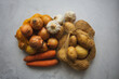 Kartoffeln, Zwiebeln und Karotten in Gemüsenetz auf einem grauen Beton HIntergrund. Draufsicht.