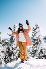 Russia. Sheregesh. Beautiful Girl in black sun goggles in winter in sunny weather outdoors among the Christmas tree and snow against blue sky. The girl is posing and smiling.