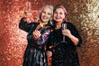 © Artem Varnitsin - Two happy senior women holding sparklers and glasses of champagne against a glitter background