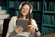 © muse studio - tablet audiobook woman wireless headphones, office workplace report place. A student with glasses in the library.